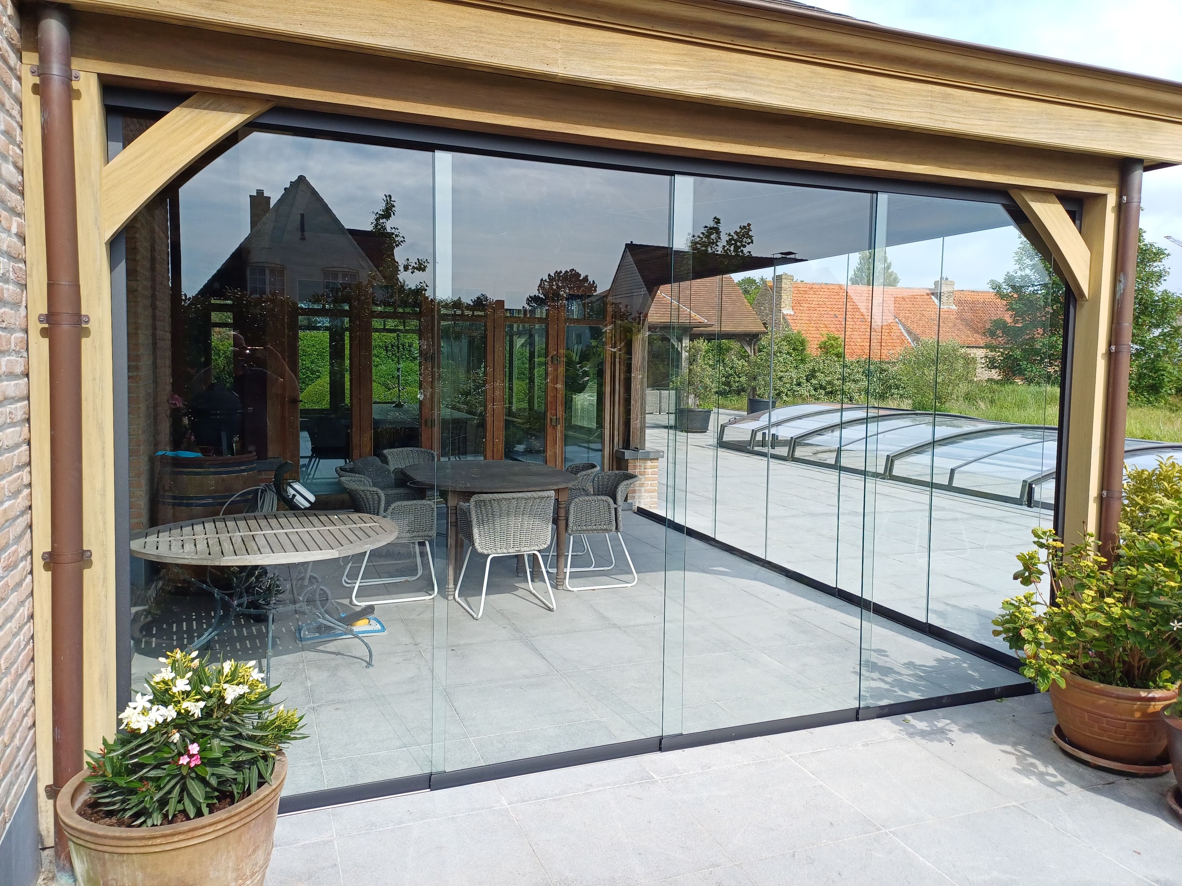 Schuifwanden onder terrasoverkapping uit hout, ter bescherming van buiteneettafel.